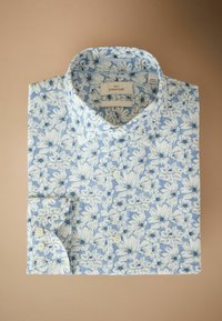 Modrý a biely kvetinový vzorovaný košeľový top starostlivo zložený s viditeľnými gombíkmi a golierom na béžovom pozadí.