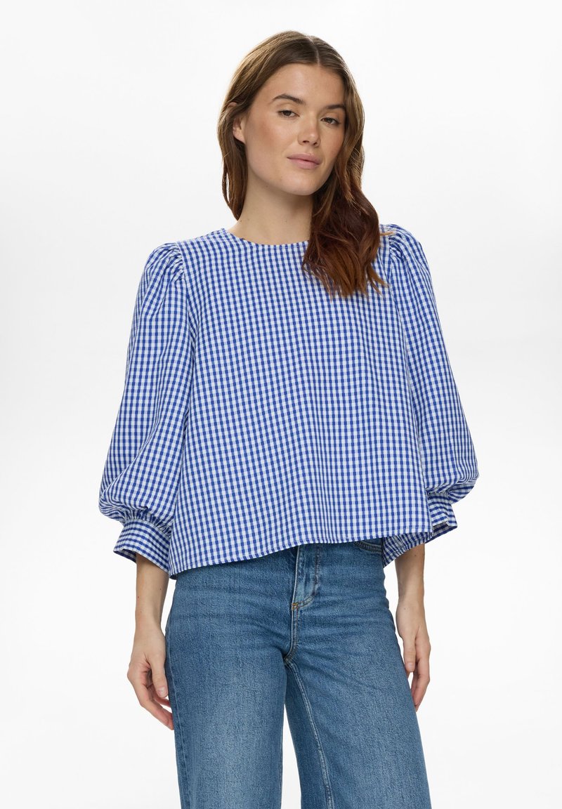 Blouse en vichy bleu et blanc avec manches bouffantes, encolure ronde et coupe décontractée. Associée à un jean taille haute bleu clair.