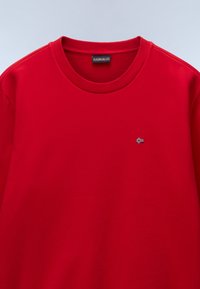 Sudadera roja con cuello redondo, cuello acanalado y un pequeño logotipo de bandera bordado en el pecho. Textura suave y diseño sencillo.