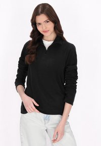 Polerón negro con media cremallera, material de forro polar suave, manga larga y corte relajado, combinado con jeans de denim azul claro.