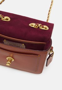 Borsa a tracolla in pelle marrone con chiusura a scatto in tonalità oro, interno in suede borgogna e tracolla in catena dorata con dettaglio in pelle.