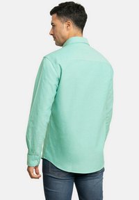 Camisa de manga larga en verde menta hecha de una tela con acabado texturizado. Presenta un cuello y puños abotonados, un dobladillo curvado y detalle en el yugo trasero.