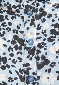 Camisa de botão azul clara com um padrão floral em preto, branco e matizes de laranja. Botões azuis notáveis acrescentam detalhe ao design.
