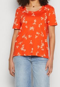 Orange kortærmet T-shirt med et blomsterdesign i off-white. Lavet af bomuldsstof med en V-halsudskæring og en afslappet pasform, der er parret med denim.