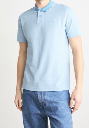 Hellblaues Poloshirt aus Baumwolle, mit einem Kragen mit weißem Rand, einer Knopfleiste mit zwei Knöpfen und dem Logo auf der linken Brustseite.