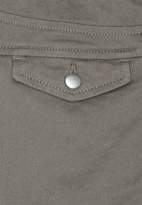 Poche en tissu gris avec un bouton-pression argenté et des détails de couture contrastés, présentant un design épuré et une texture lisse.