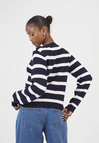Pull en maille rayé bleu marine et blanc avec des manches longues et un col arrondi, associé à un jean en denim bleu clair taille haute.