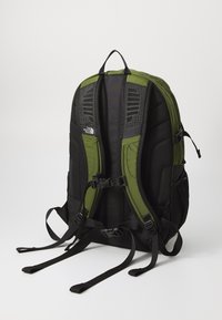 Sac à dos noir et vert olive avec des panneaux en maille, des bretelles ajustables et des poches latérales. Il est doté d'un dos rembourré et d'un label de marque.