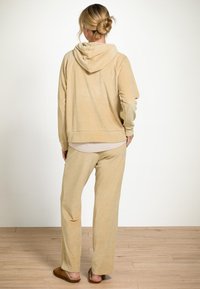 Beige hoodie met een relaxte pasvorm, gecombineerd met bijpassende wijde broek. Zachte textuur, minimaal ontwerp en subtiele details.
