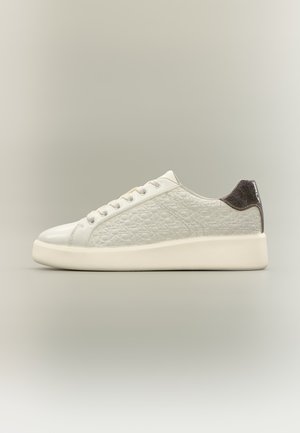 Baskets basses blanches avec motif embossé, lacets blancs, semelle épaisse et accent métallique foncé au talon, vues de profil sur fond neutre.
