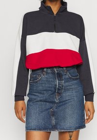 Sweatshirt à demi-fermeture éclair en blocs de couleurs bleu marine, blanc et rouge ; tissu doux. Associé à une mini-jupe en jean bleu avec une couture frontale.