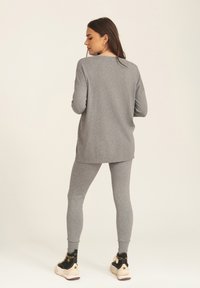 Grey long-sleeve top and matching leggings made of soft material, featuring a relaxed fit. The outfit is complemented by black sneakers.