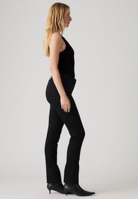 Pantalones vaqueros skinny negros de mezclilla, con una cintura alta, diseño de cinco bolsillos y costuras mínimas. Combinados con una camiseta sin mangas negra y botas hasta el tobillo.