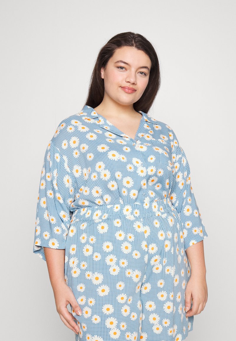 Vestido azul com padrão e anos de flores amarelas e brancas, corte solto, mangas curtas e cintura elástica. Textura do tecido suave.