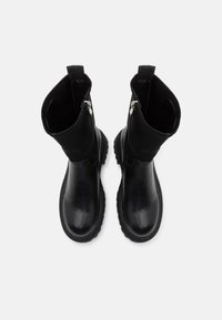 Botas de cuero negras hasta el tobillo con un acabado suave, punteras redondeadas y paneles laterales texturizados. Cuentan con cremalleras y lengüetas para ponerlas y quitarlas con facilidad.