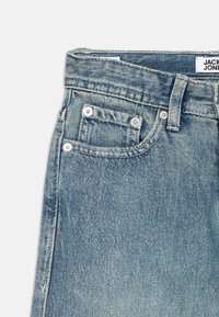 Ανοιχτό μπλε τζιν με κλασικό σχεδιασμό, πέντε τσέπες, εμφανείς ραφές και ετικέτα του εμπορικού σήματος στη μέση.