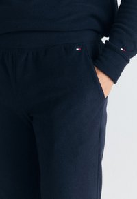 Tmavě modrá fleecová mikina a tepláky s jemnou texturou; obsahují logo v červené a bílé barvě na rukávu a pase.