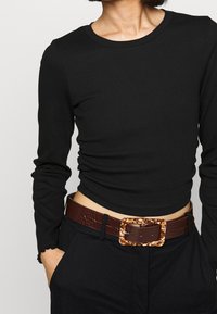 Černý dlouhý rukáv žebrový top s kulatým výstřihem, doplněný tmavě hnědým páskem s texturou krokodýlí kůže a masivní sponou se vzorem.