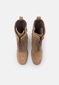 Botas de tobillo de ante color beige con un forro suave, cordones planos y ojales dorados. Presentan un cierre lateral y una suela con costuras blancas en contraste.