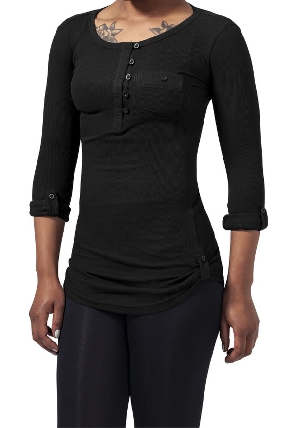 Kobieta ubrana w czarną koszulkę typu henley z rękawami do łokcia, ozdobioną guzikami, z kieszenią na piersi i podwiniętymi mankietami, w połączeniu z czarnymi spodniami.