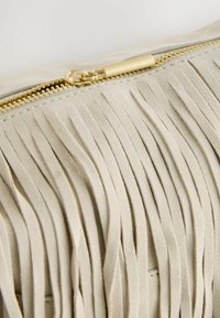 Beige ruskind clutch med vertikale frynser, guld lynlåsdetaljer og glat tekstur. Har et rent design med detaljeret syning.