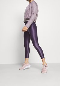 Fioletowe legginsy o błyszczącym wykończeniu, w połączeniu z jasnofioletową kurtką typu bomber oraz r�óżowymi butami sportowymi z białymi podeszwami.