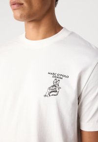 Witte katoenen t-shirt met een zwart bedrukt beer die gitaar speelt, met boven de afbeelding de tekst "MARC O'POLO DENIM" op de linkerborst.