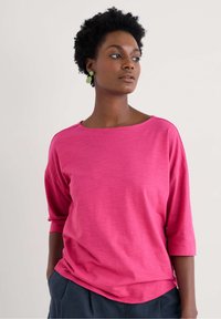 Fuchsia pink, loose-fitting top made of lightweight fabric, featuring three-quarter sleeves and a wide neckline, with subtle texture.