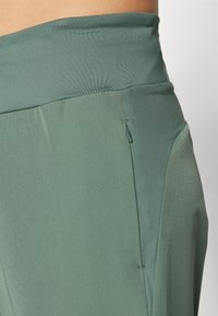 Aukščiausiais liemeniu žali kelnių, pasižyminčių švelnia tekstūra, elegantišku dizainu ir kampiniu užtrauktuko kišeniu šone funkcionalumui.