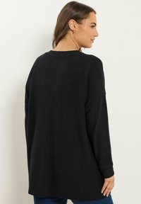 Pull noir à manches longues avec une coupe décontractée, tissu texturé, poignets côtelés et encolure arrondie, présentant un détail de couture droite au dos.