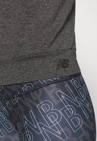 Tumma harmaa urheilupaita, jossa on neulottu rakenne, yhdistettynä laivastonsinisiin legginsseihin, joissa on valkoisia "NB"-logokuvioita.