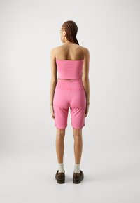 Ružový crop top a zodpovedajúce cyklistické šortky vyrobené z elastického materiálu, s priliehavým strihom. Nosené s hnedými platformovými topánkami a bielymi ponožkami.