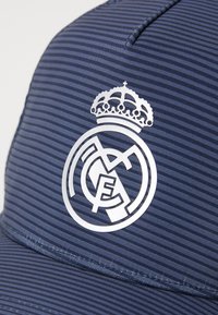 Navy cap featuring a striped texture and a prominent silver Real Madrid logo with a crown above it, designed for casual wear.