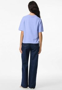 Gaiši purpursarkans īsām piedurknēm tops ar brīvu piegriezumu, apvienots ar tumši ziliem platiem džinsiem. Gluda kokvilnas tekstūra, minimālas dizaina detaļas.