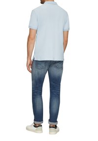 Jasnoniebieska koszulka polo z krótkim rękawem, zestawiona z ciemnoniebieskimi zwężanymi dżinsami i białymi trampkami, widok od tyłu.