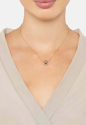 Gold necklace with a circular pendant featuring a bee design, surrounded by small clear stones, worn against a light-colored top.