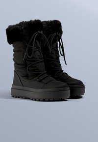 Czarne ocieplane botki z mankietem z imitacji futra, wiązane na sznurowadła, z grubą gumową podeszwą i wyściełanym wnętrzem dla zwiększenia ciepła i komfortu.