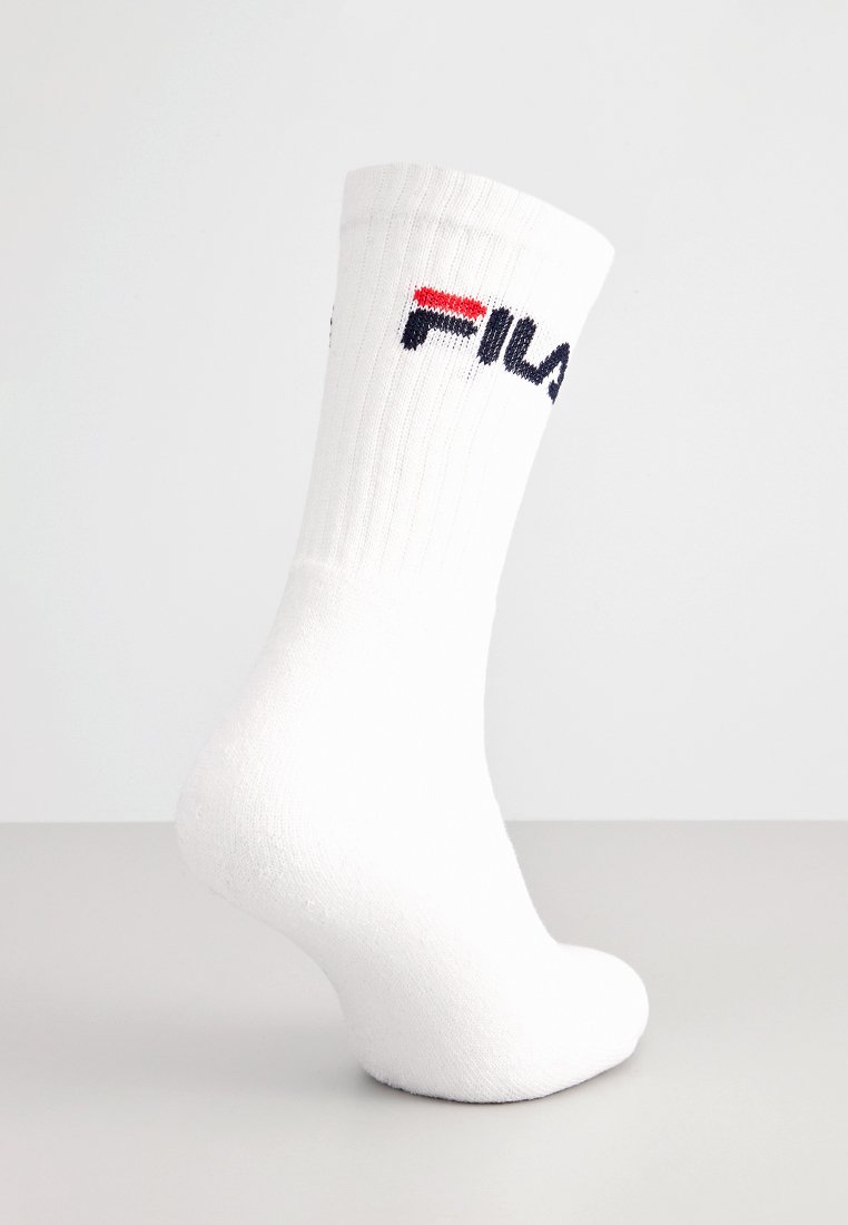 Biała skarpeta za kostkę z ribbowanym mankietem, z logo FILA w kolorach czerwonym, czarnym i granatowym na jasnoszarym tle.