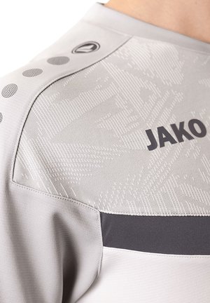Grijze sporttrui met een textuurpatroon en contrasterende donkergrijze accenten. Bevat ronde geperforeerde gaten op de schouder. Merkennaam "JAKO" zichtbaar.