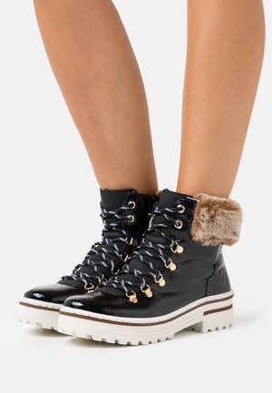 Stivali stringati in vernice nera con suole bianche e polsini in pelliccia sintetica color cuoio indossati su gambe nude.