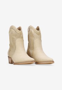 Botines beige de ante con lados perforados, punta afilada y tacón bajo apilado. Presenta una cremallera lateral para facilitar su uso.