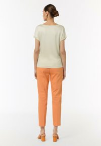 Jasnozielony top z krótkim rękawem o luźnym kroju, zestawiony z pomarańczowymi zwężanymi spodniami. Gładka tkanina z minimalistycznym designem; widoczne detale szwów.