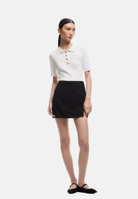 Valkoinen ribbed polo-paita lyhyillä hihoilla ja kolmella kultaisella napilla, yhdistetty mustaan mini-hameeseen ja mustiin ballerinoihin. Yhteensopiva sileä rakenne.