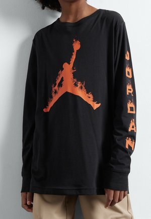 Chemise noire à manches longues en coton, arborant un logo Jumpman orange flamboyant sur le devant et le texte "JORDAN" le long de la manche gauche.