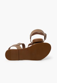Brown strappy sandals feature a flat sole with a textured rubber surface, adjustable ankle strap, and a minimalist design. Size 35 noted on the sole.