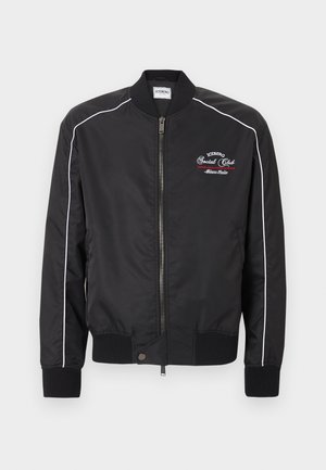 Czarna kurtka bomberka z przednim zamkiem błyskawicznym, białym obszyciem na rękawach, ściągaczami na mankietach i dole oraz białoczerwonym haftowanym napisem na lewej piersi.