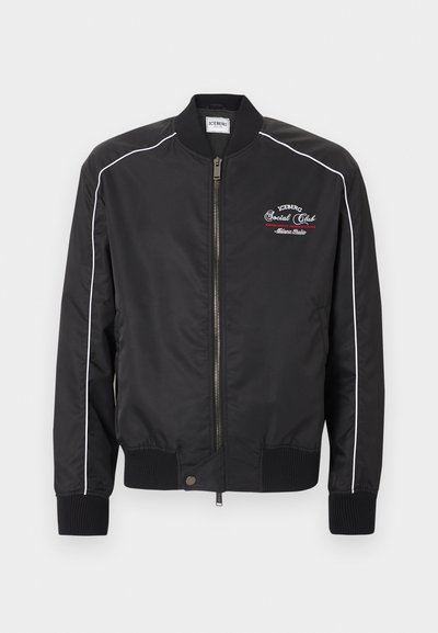 Μαύρο μπουφάν bomber με φερμουάρ μπροστά, λευκή λεπτομέρεια κατά μήκος των μανικιών, ριμπ μανσέτες και τελείωμα, και λευκό-κόκκινο κεντητό κείμενο στο αριστερό μέρος του στήθους.