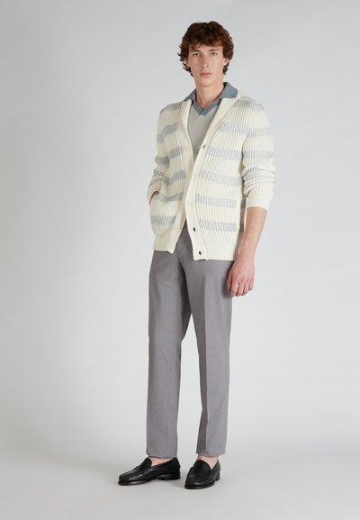 Cardigan lavorato a maglia color crema con strisce grigie, abbinato a pantaloni grigi su misura e mocassini neri. Presenta una vestibilità rilassata e chiusura con bottoni.