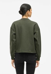 Īss zaļš sporta krekls ar apaļu kakla izgriezumu un pazeminātām plecu šuvēm. Izgatavots no mīkstas auduma, tam ir ribotas aproces un elastīga apakšmala.