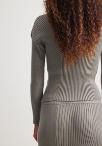 Graues, geripptes Strickkleid mit taillierter Silhouette, langen Ärmeln und einem gespaltenen Saum, das eine weiche Textur und vertikale Linien zeigt.